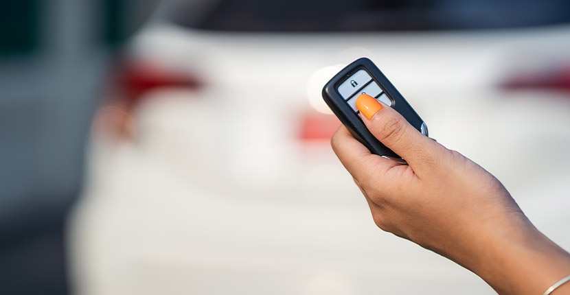 Person clicking a key fob behind a white vehicle