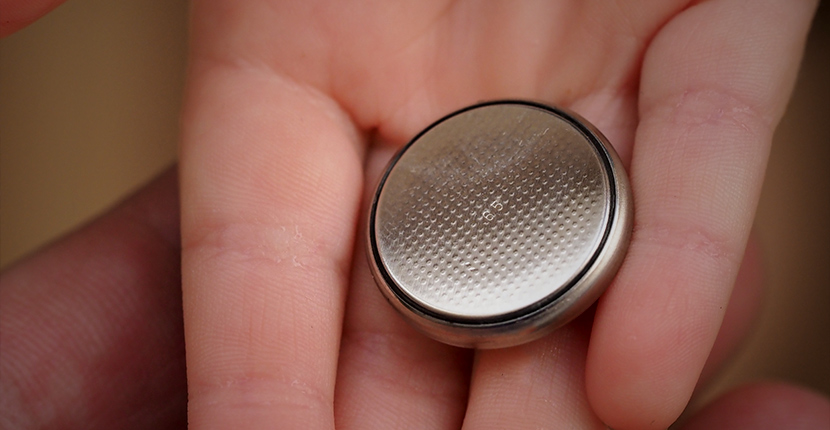 A hand holding a coin cell battery