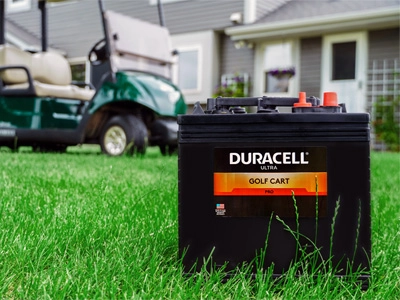 Golf cart battery on grass with a golf cart and house behind it