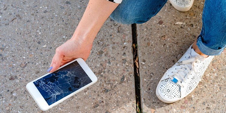 woman picking up a phone from the sidewalk with a cracked screen