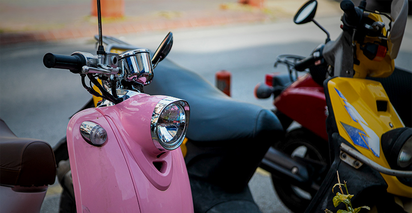 A pink, yellow and red scooter or moped parked in a row