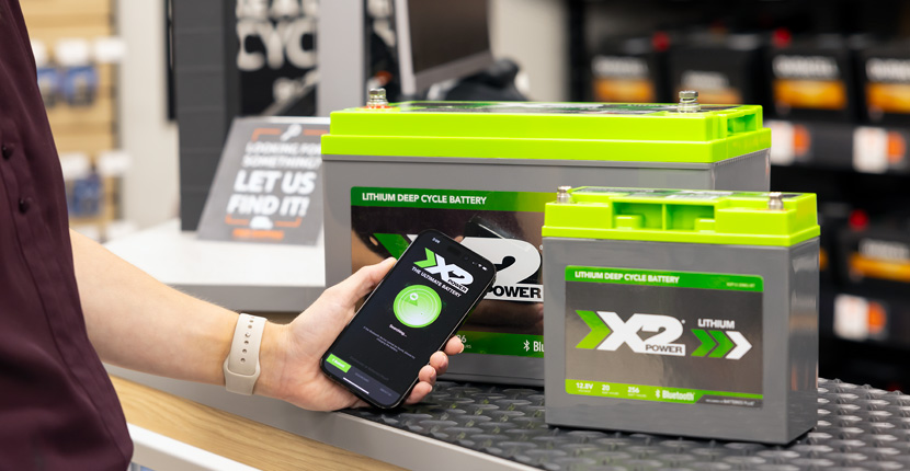 Two X2Power Marine batteries with Bluetooth and someone holding a phone with the app