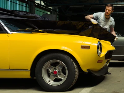 A guy putting a cover on a classic car