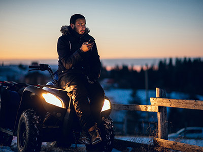 Guy on his phone sitting on the front of an ATV near a fence