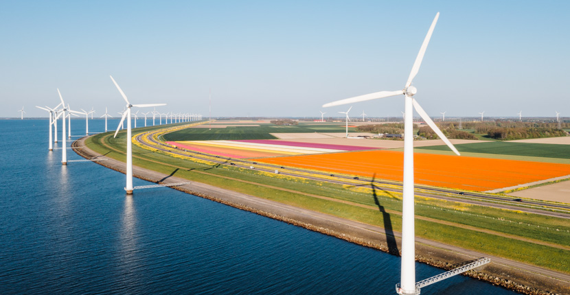 Wind turbines on water near farm land with other turbines in the background
