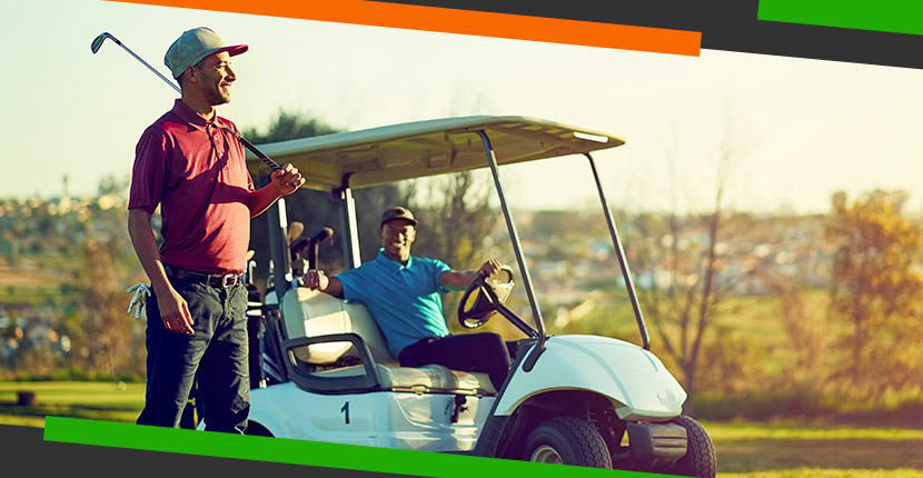 Man standing next to golf cart with a club while another man sitting in drivers seat