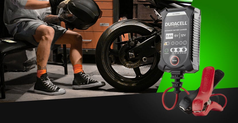 Man sitting on a bench wiping his helmet with the rear wheel of a motorcycle - close up of a Duracell battery charger