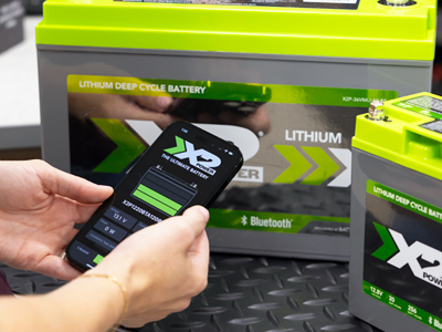 person looking at an app on a phone in front of 2 X2Power batteries