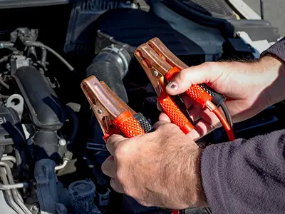 Holding jumper cables in front of a vehicle battery