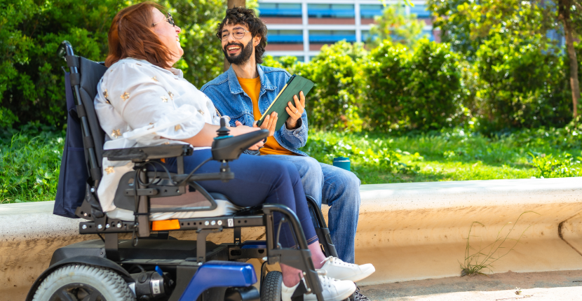 Person in an electric wheelchair talking to someone sitting on a bench