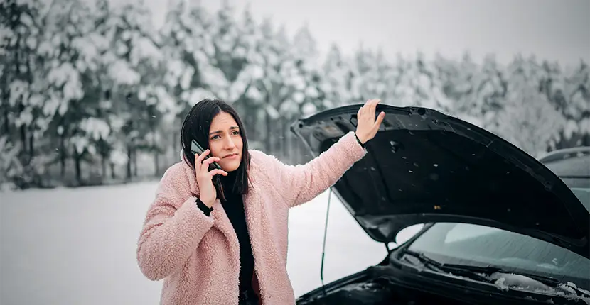 Woman on the phone standing in front of a car with the hood up