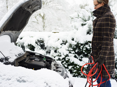 person standing at the front of a car with the hood up holding jumper cables