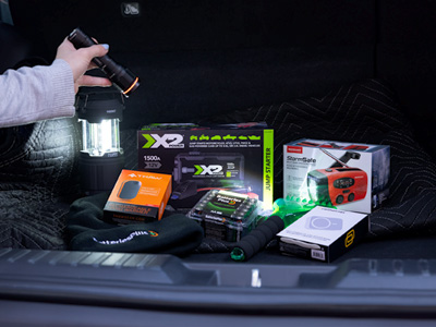 A person shining a flashlight on emergency products in the trunk of a vehicle.
