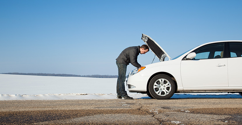 Man looking under the hood of a white car on the side of the road