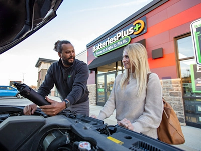 A store employee checking an auto battery while talking to the car owner.