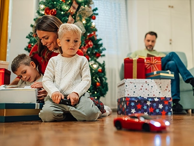 Child playing with a remote controlled vehicle with family in the background